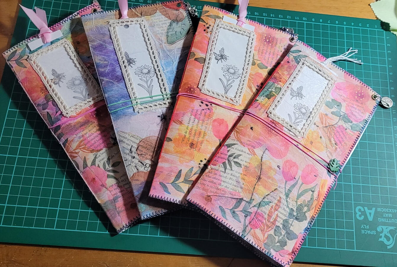 Final stage. These journals have had their cover dangles added, their elastic closures secured, and their cute little flower tags added to peek through the window part of the original envelope.